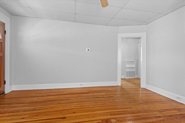 spare room with visible vents, a ceiling fan, wood finished floors, a paneled ceiling, and baseboards