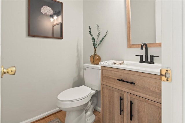 half bath with toilet, vanity, baseboards, and wood finished floors