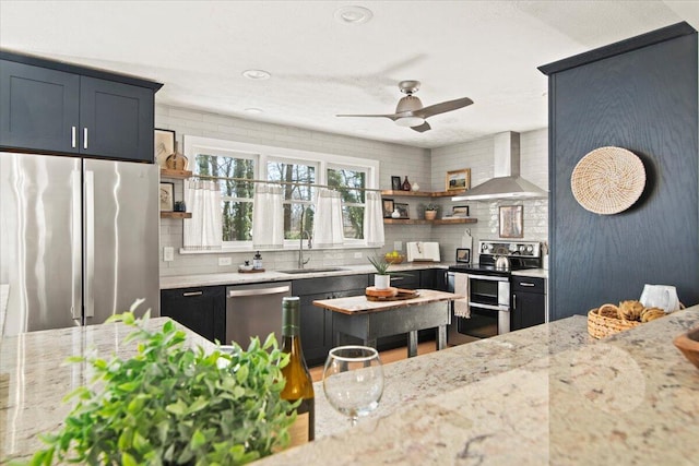 kitchen featuring a ceiling fan, open shelves, a sink, stainless steel appliances, and wall chimney exhaust hood