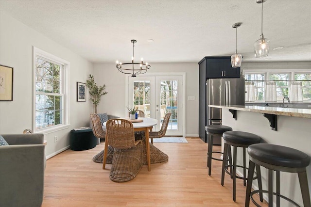 dining space featuring light wood-style flooring, a notable chandelier, french doors, and baseboards