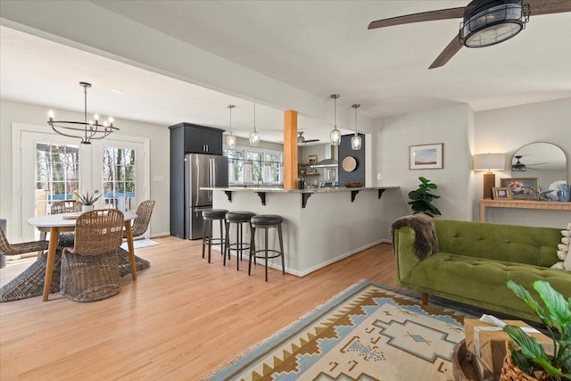 living room with ceiling fan with notable chandelier, light wood-type flooring, and baseboards