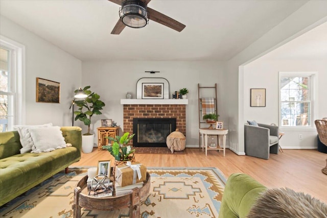 living area featuring baseboards, wood finished floors, a brick fireplace, and ceiling fan