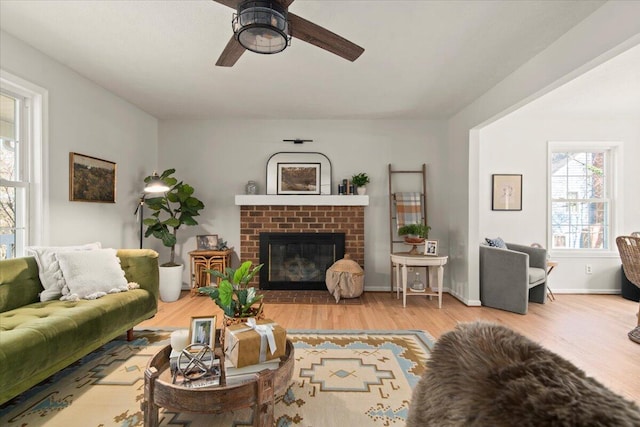 living area with wood finished floors, a brick fireplace, a ceiling fan, and baseboards