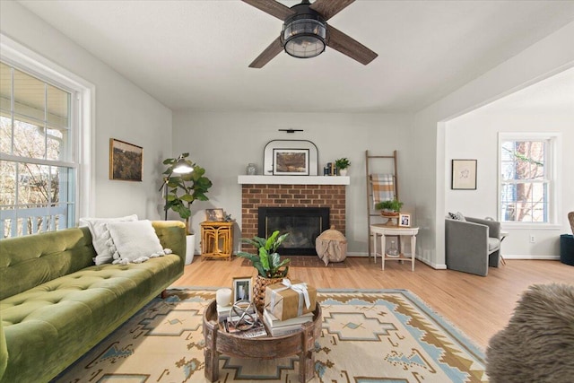 living room featuring wood finished floors, a brick fireplace, a ceiling fan, and baseboards