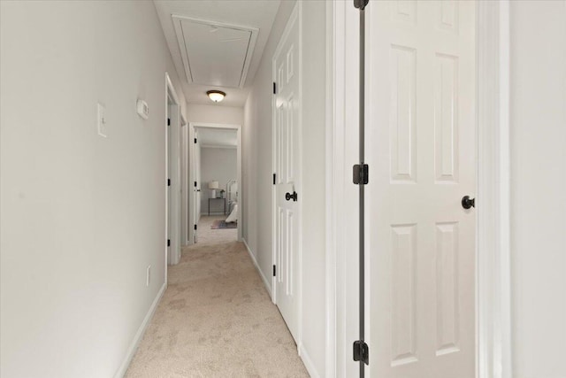 hallway with attic access, baseboards, and light carpet