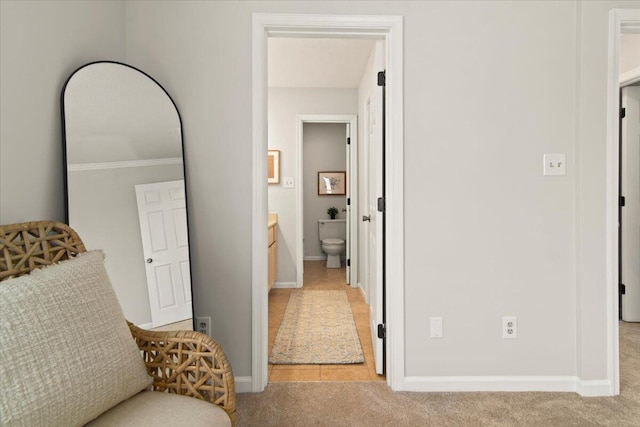 hallway with baseboards and light colored carpet