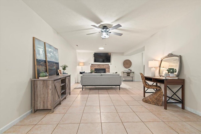 living room featuring light tile patterned flooring, a brick fireplace, baseboards, and ceiling fan