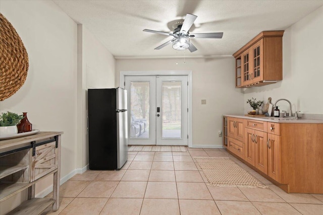 kitchen featuring a sink, freestanding refrigerator, french doors, light tile patterned flooring, and glass insert cabinets