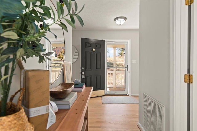 foyer entrance featuring visible vents, a textured ceiling, and wood finished floors