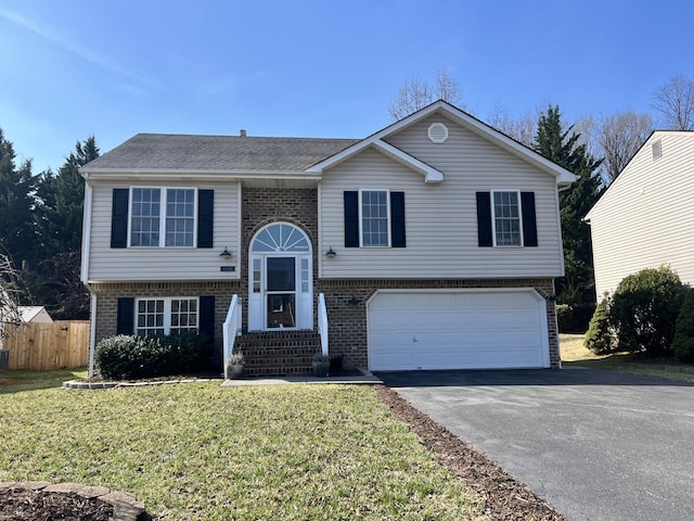 raised ranch with a front yard, fence, driveway, a garage, and brick siding