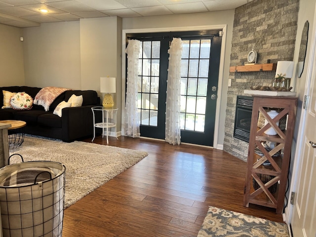 living area with a fireplace, wood finished floors, baseboards, and a drop ceiling