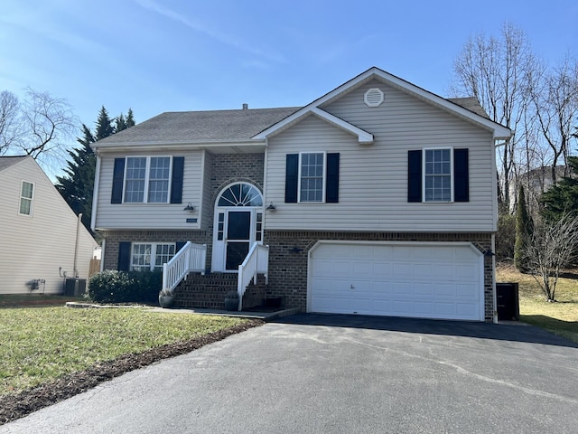 raised ranch with brick siding, central AC unit, an attached garage, and aphalt driveway