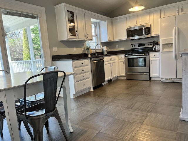 kitchen with dark countertops, appliances with stainless steel finishes, white cabinetry, and glass insert cabinets