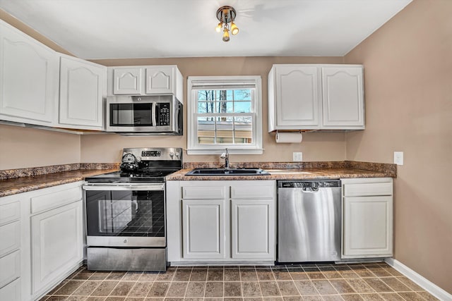 kitchen featuring baseboards, a sink, stainless steel appliances, white cabinets, and dark countertops