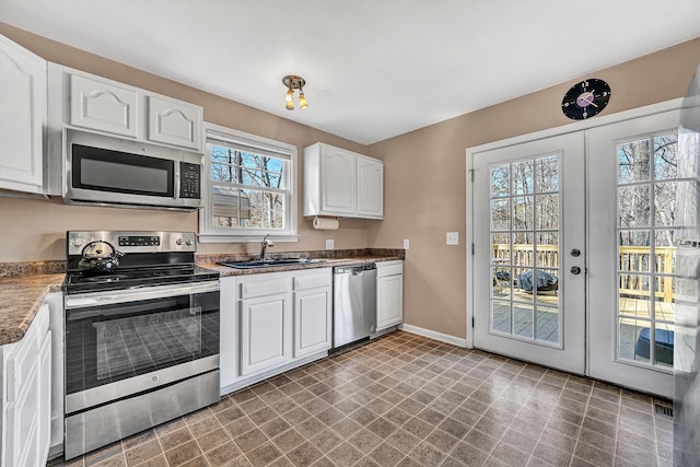 kitchen featuring baseboards, appliances with stainless steel finishes, french doors, white cabinets, and a sink