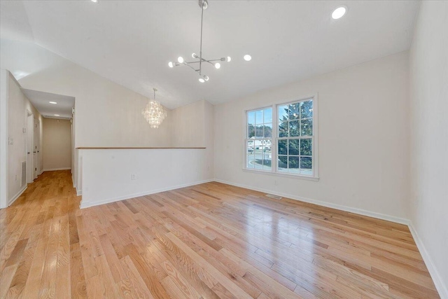 empty room featuring light wood-type flooring, visible vents, lofted ceiling, an inviting chandelier, and baseboards