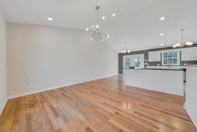 unfurnished living room with a notable chandelier, lofted ceiling, a sink, light wood finished floors, and baseboards