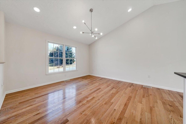 empty room featuring baseboards, lofted ceiling, a notable chandelier, and light wood finished floors