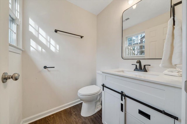 half bathroom with visible vents, baseboards, toilet, wood finished floors, and vanity