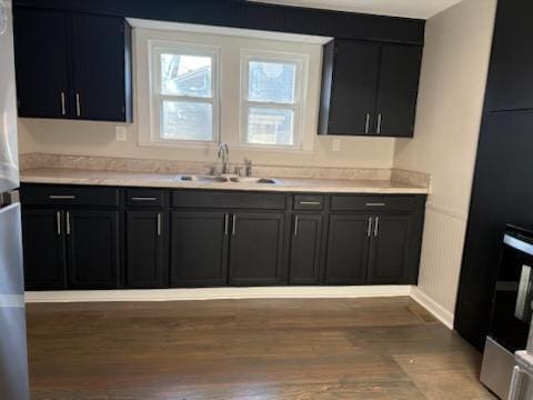 kitchen with a sink, freestanding refrigerator, light wood-style floors, light countertops, and dark cabinets