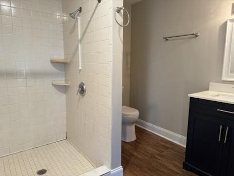 bathroom with baseboards, toilet, vanity, and a tile shower