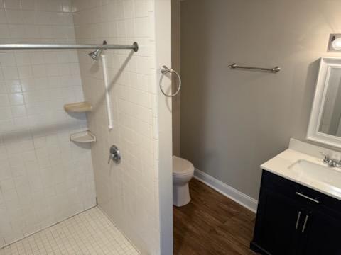 full bath with vanity, wood finished floors, baseboards, a tile shower, and toilet