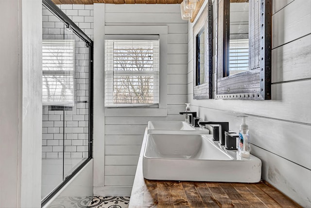 bathroom featuring combined bath / shower with glass door, wood walls, and a sink