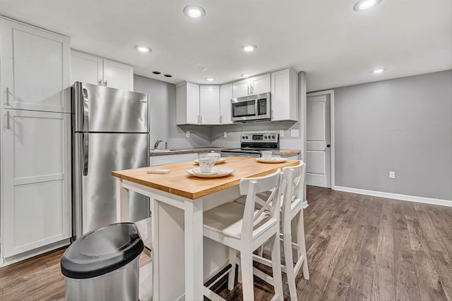 kitchen with wooden counters, a breakfast bar, dark wood finished floors, white cabinets, and appliances with stainless steel finishes