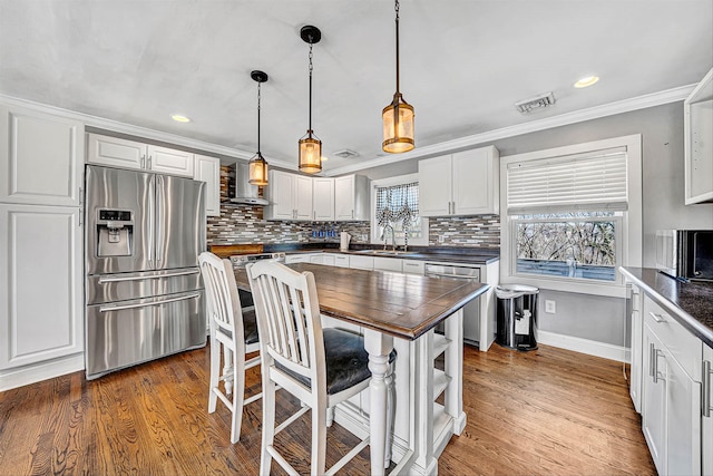 kitchen with crown molding, wall chimney range hood, visible vents, and stainless steel appliances