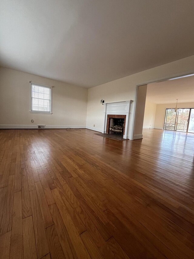 unfurnished living room with visible vents, a brick fireplace, dark wood-type flooring, and baseboards