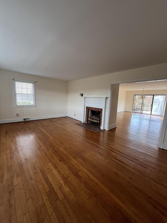 unfurnished living room with visible vents, baseboards, a brick fireplace, and dark wood-style flooring