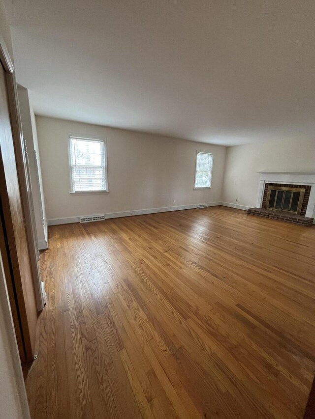 unfurnished living room with a brick fireplace, plenty of natural light, wood finished floors, and visible vents