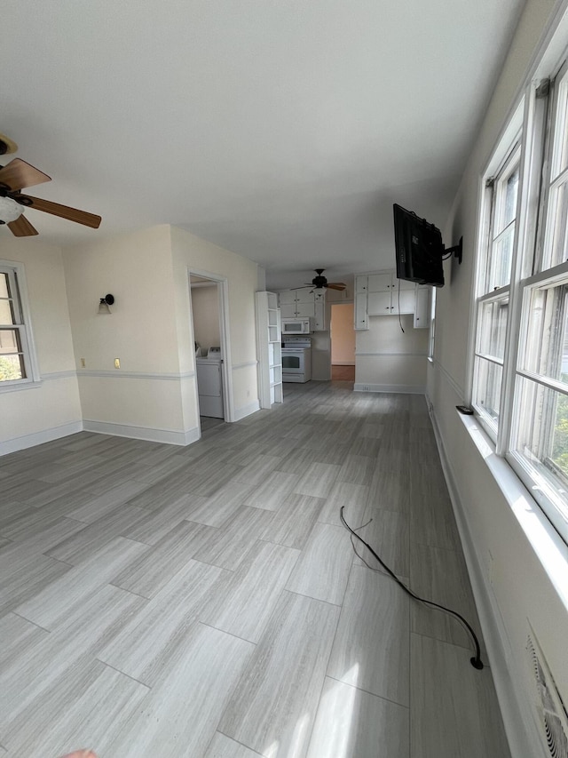 unfurnished living room featuring a ceiling fan, a healthy amount of sunlight, baseboards, and washing machine and clothes dryer