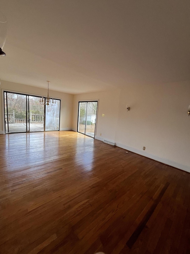 empty room featuring visible vents, baseboards, wood finished floors, and a chandelier