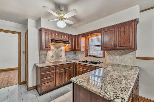 kitchen with light stone countertops, a peninsula, a sink, under cabinet range hood, and black electric cooktop