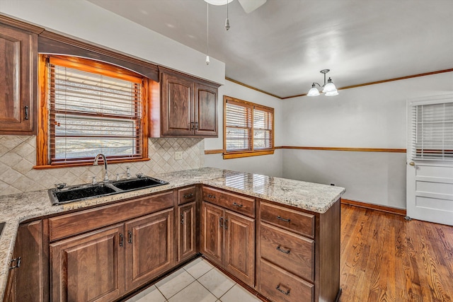 kitchen with light wood-type flooring, ornamental molding, a sink, backsplash, and a peninsula