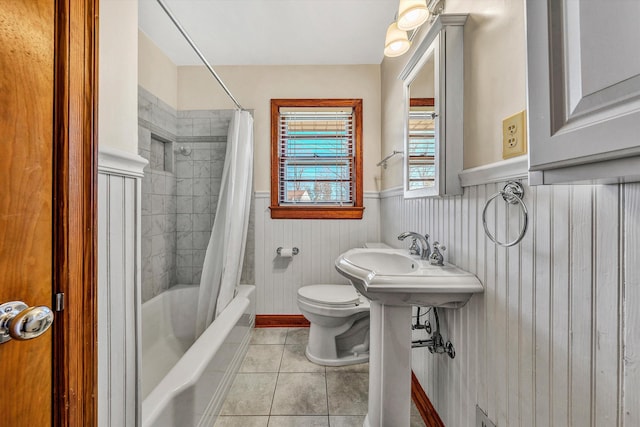 bathroom featuring tile patterned floors, toilet, shower / bathtub combination with curtain, and a wainscoted wall