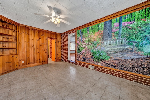 empty room with wooden walls, visible vents, brick wall, and a ceiling fan