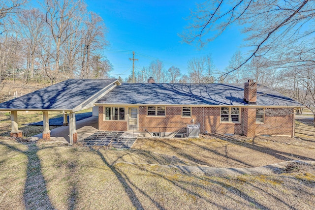 back of property featuring brick siding, a shingled roof, cooling unit, a chimney, and a carport