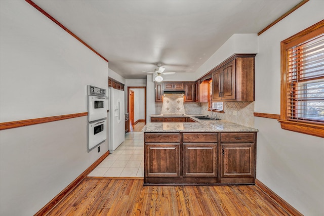 kitchen featuring light wood-type flooring, under cabinet range hood, backsplash, white appliances, and a peninsula