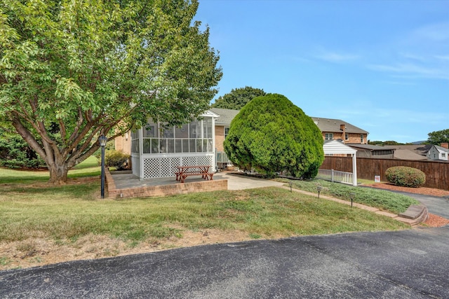 view of property hidden behind natural elements featuring a front lawn, fence, a sunroom, and a patio