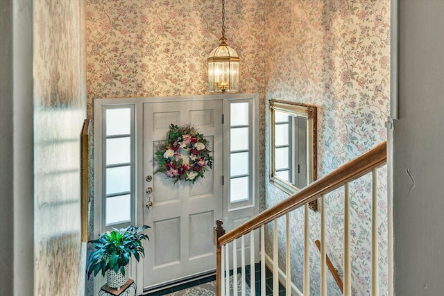 foyer with a notable chandelier, a healthy amount of sunlight, wallpapered walls, and stairs