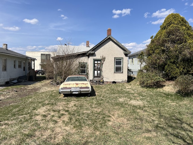 back of house with stucco siding, a chimney, and a yard