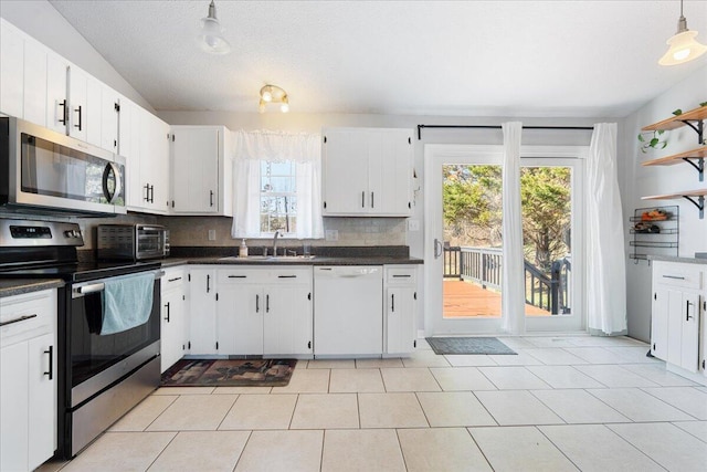 kitchen featuring dark countertops, a sink, backsplash, stainless steel appliances, and open shelves