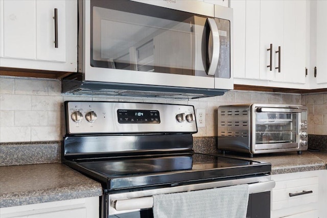 kitchen with backsplash, dark countertops, appliances with stainless steel finishes, white cabinets, and a toaster