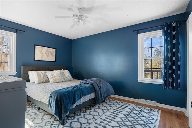 bedroom featuring multiple windows, wood finished floors, visible vents, and baseboards