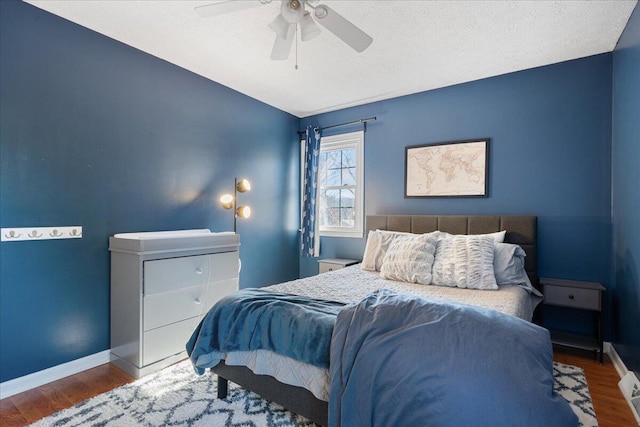 bedroom featuring a ceiling fan, visible vents, wood finished floors, baseboards, and a textured ceiling