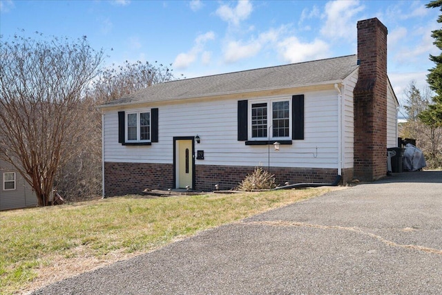 raised ranch with brick siding, driveway, a front lawn, and a chimney