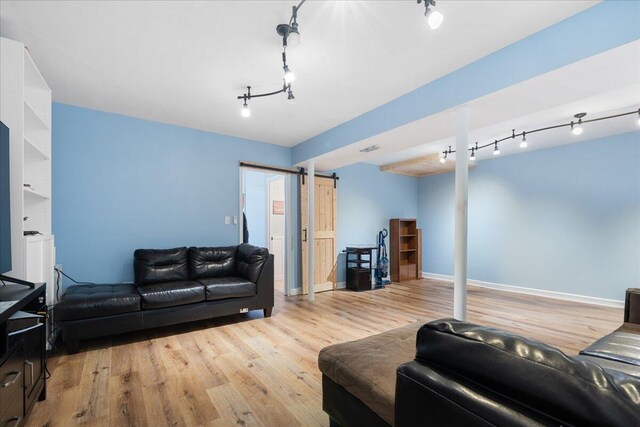 living area featuring a barn door, track lighting, baseboards, and wood finished floors