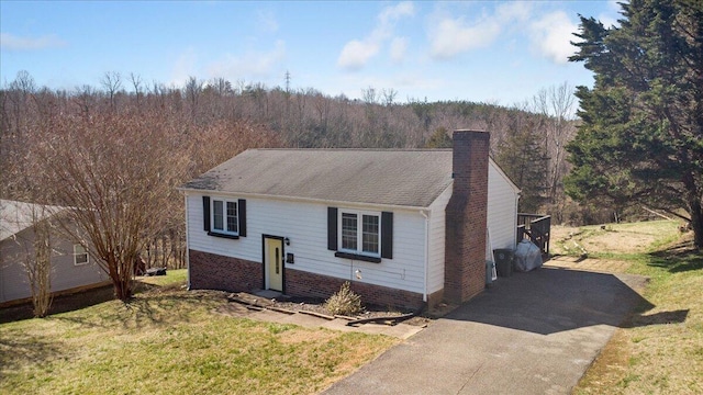 raised ranch with a front yard, a view of trees, driveway, and a chimney